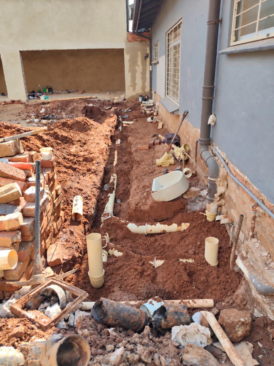 Trench with old drain pipes removed and new PVC drain lines laid